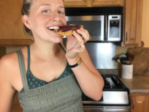 woman eating a peanut butter and jelly toast and smiling
